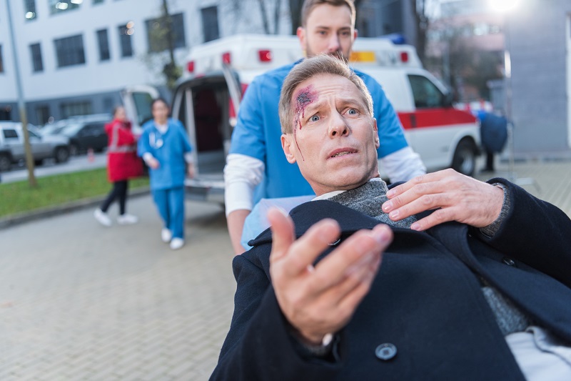 scared injured man with wound on head lying on ambulance stretcher