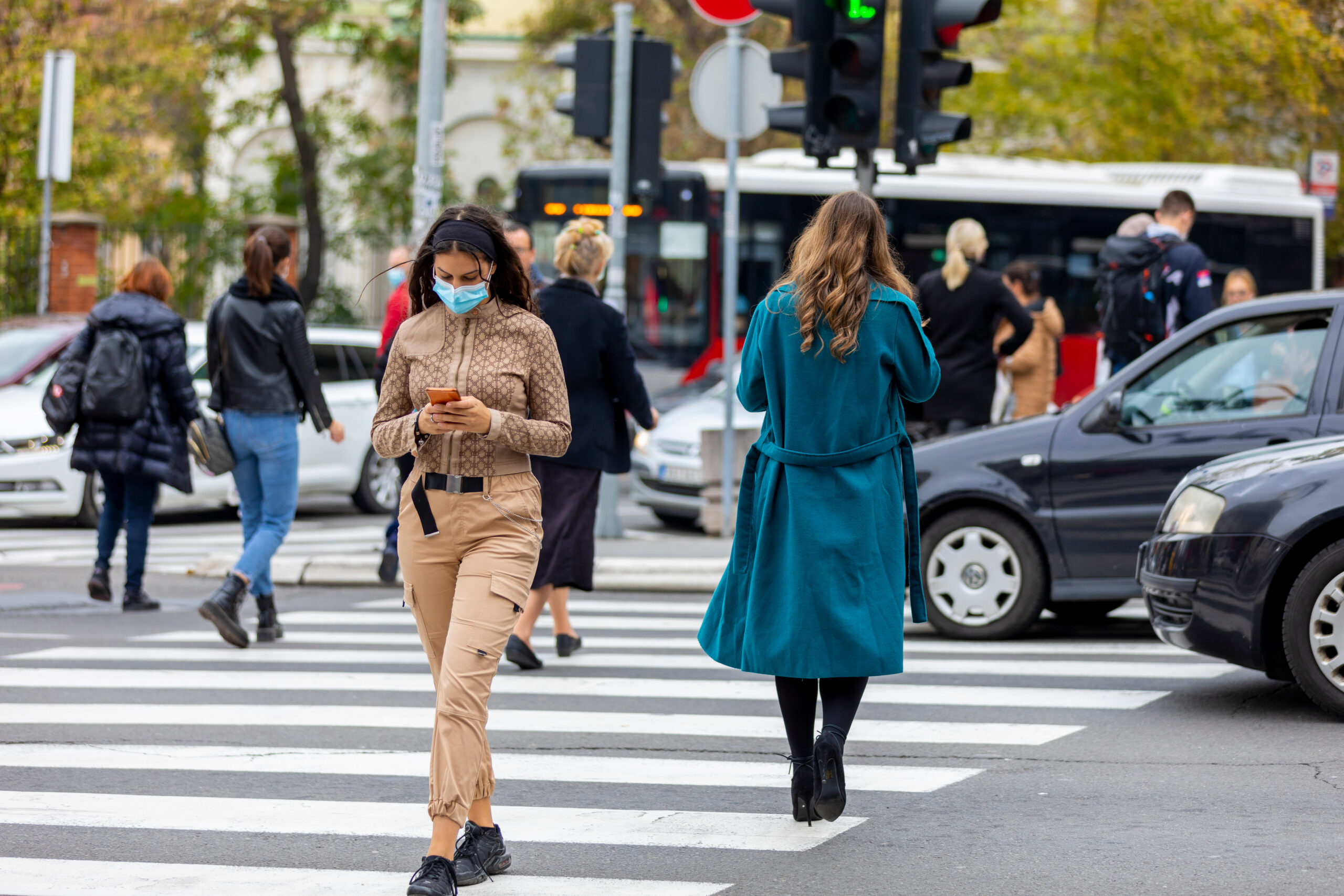 woman wearing face mask crossing street using phone
