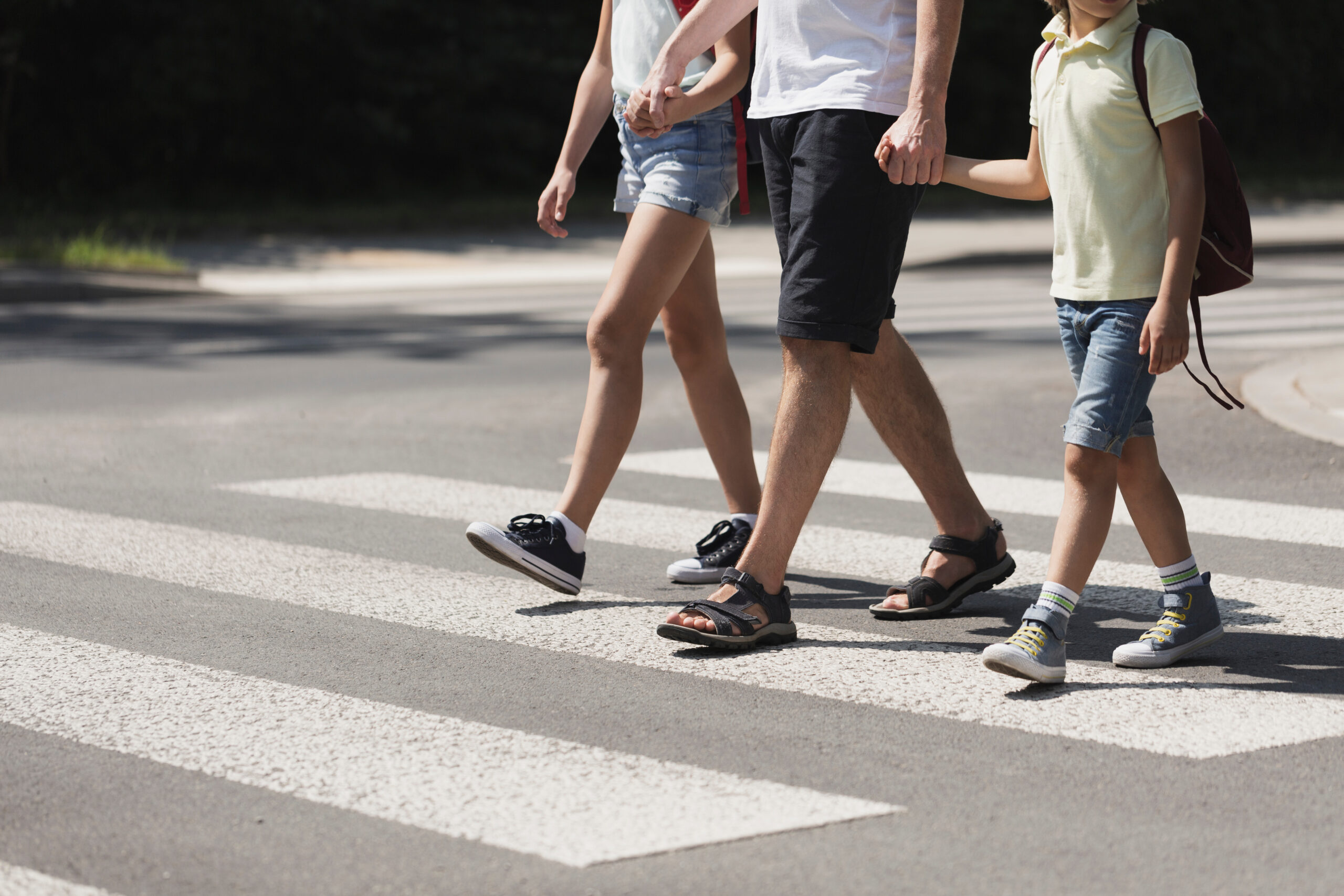 father holding hands with his kids while on pedestrian crossing